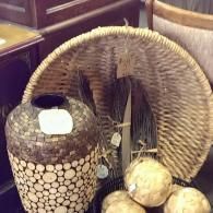 A textured cylindrical vase with wood slices, a large woven fan, feathers, and light-colored round decorative orbs.