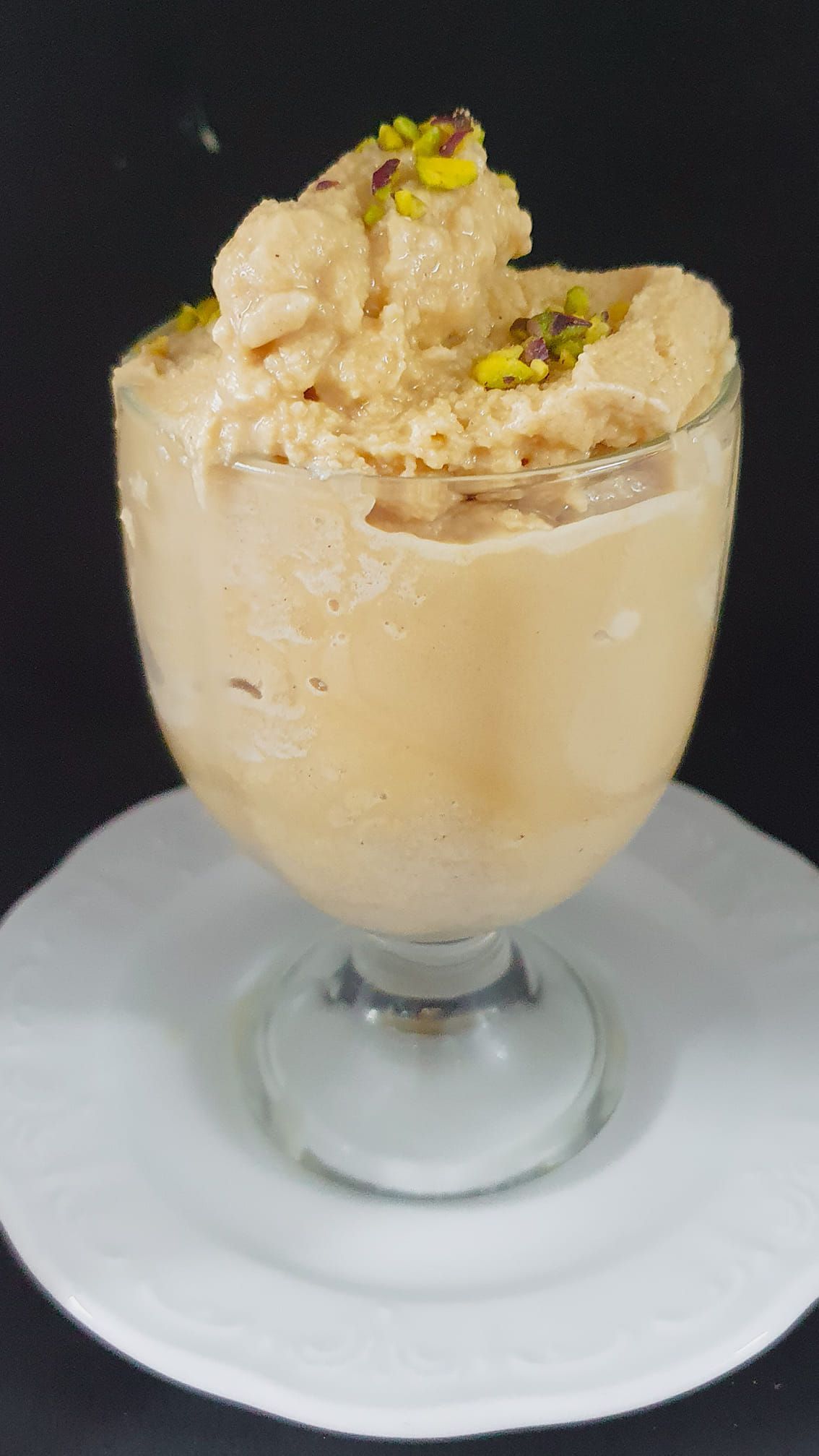 Un bicchiere di gelato con pistacchi sopra è su un piatto bianco.