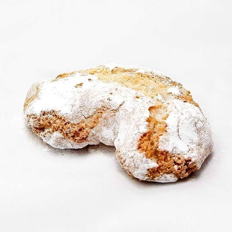 Primo piano di un biscotto ricoperto di zucchero a velo su una superficie bianca.