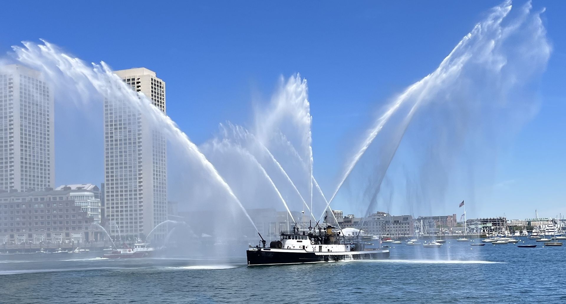 Black and white tugboat on water, spraying water from hoses. Russian flag on side.