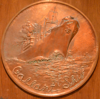 Bronze circular relief of a ship at sea, waves crashing around the hull. Text reads Bronze circular relief of a ship at sea, waves crashing around the hull. Text reads
