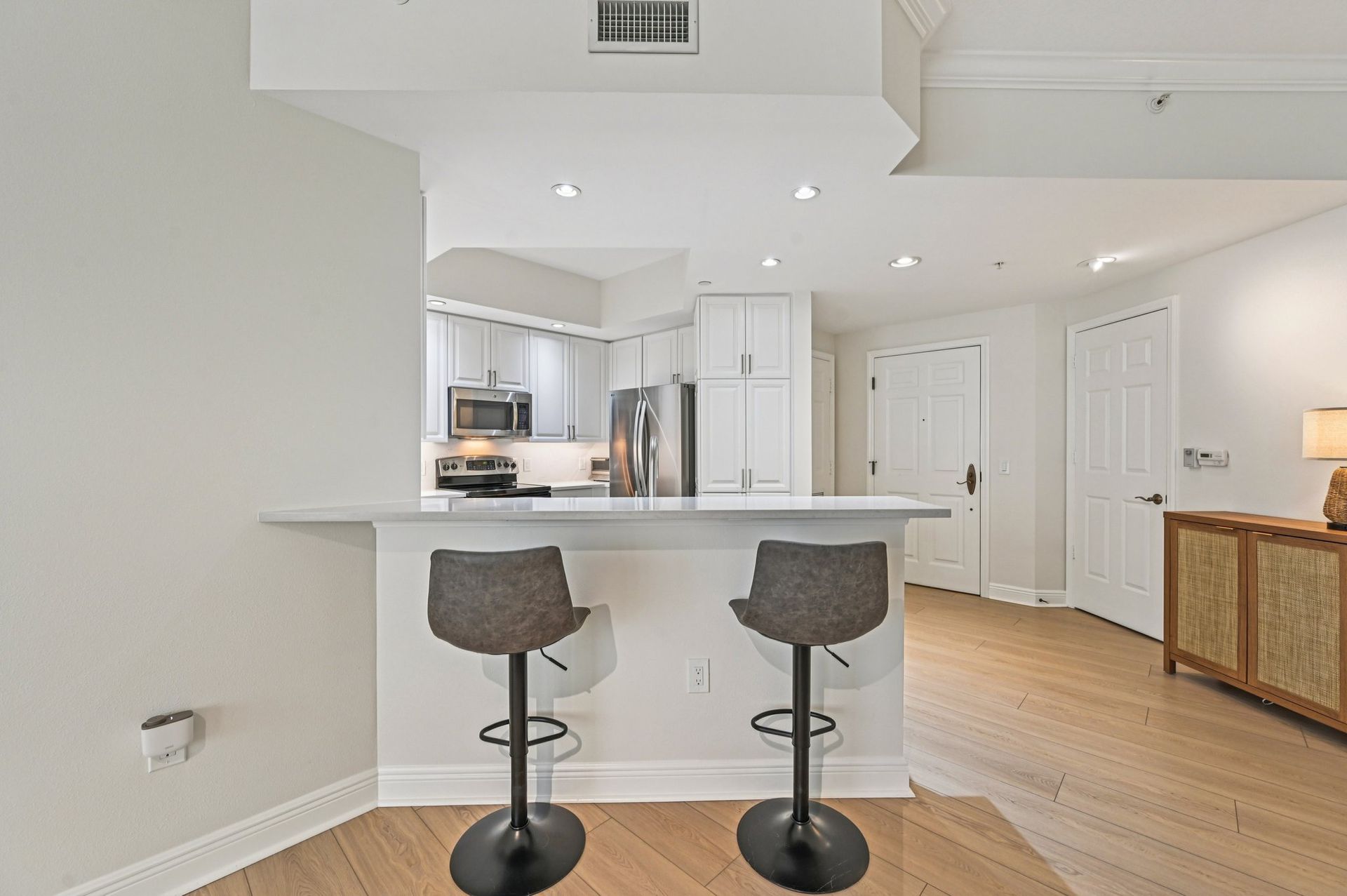Open-concept kitchen with a breakfast bar, two bar stools, and light wood flooring.