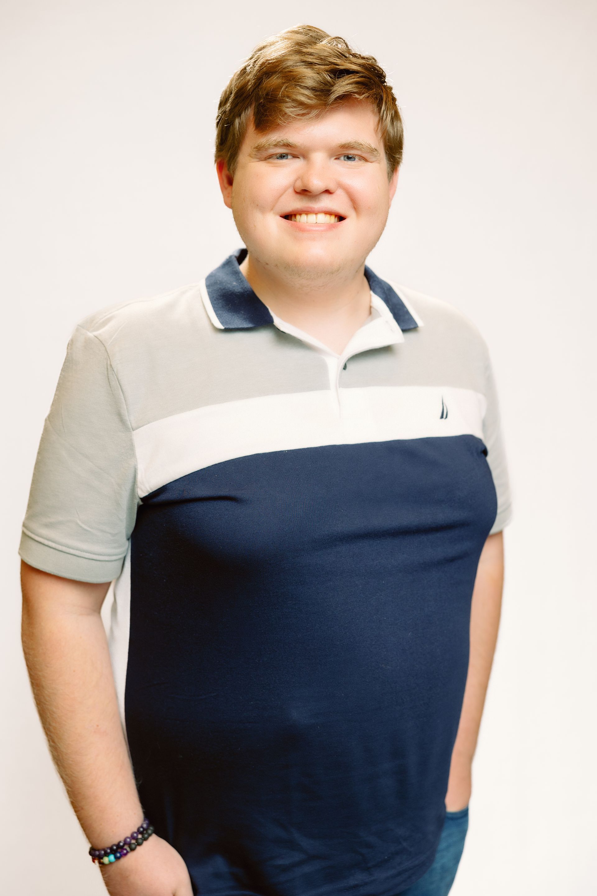 Smiling person in blue, white, and gray polo shirt poses against a white backdrop.