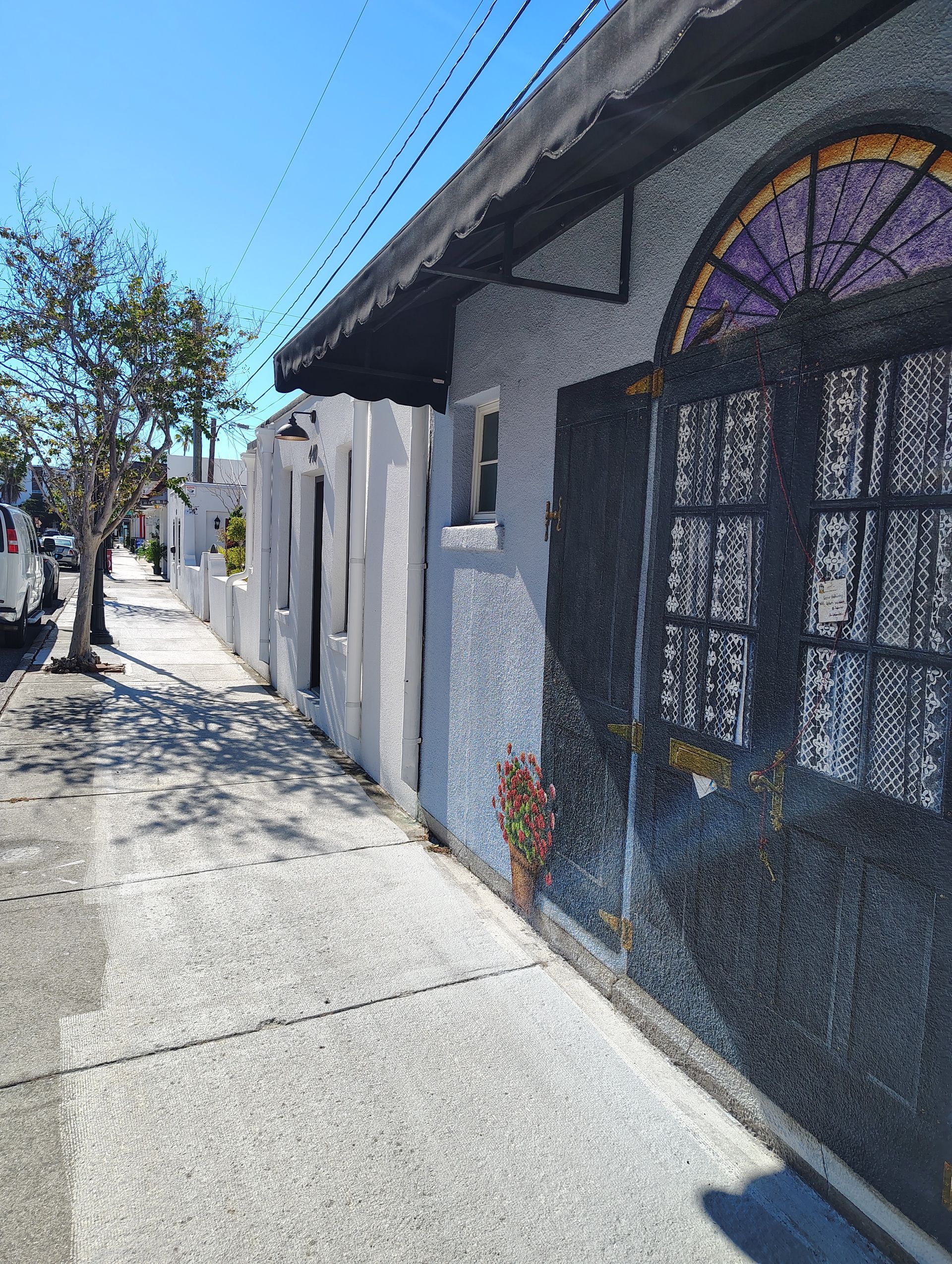 Sidewalk next to a gray stucco building with a black gate under a blue sky.