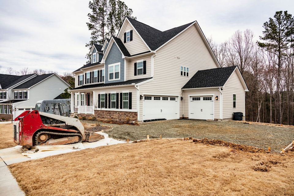 A house is being built in a residential area and a bulldozer is parked in front of it.