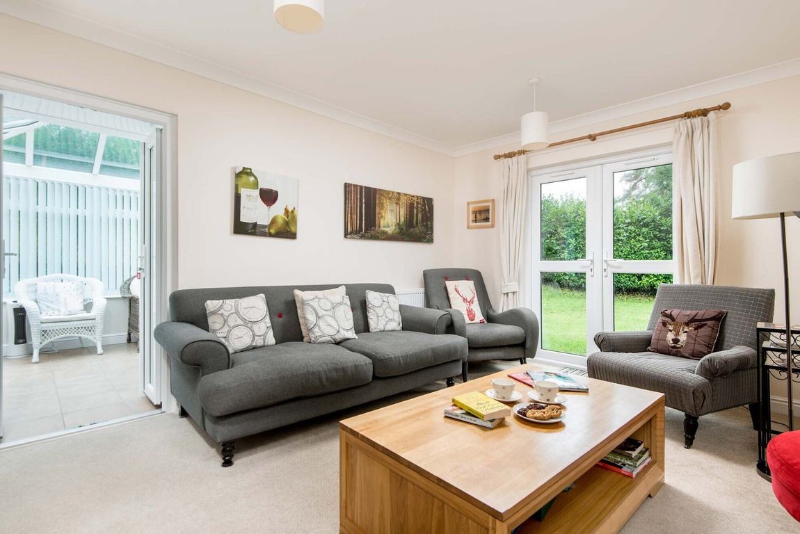 A lounge with grey handsome sofas and chairs with coffee table and patio doors leading to the garden