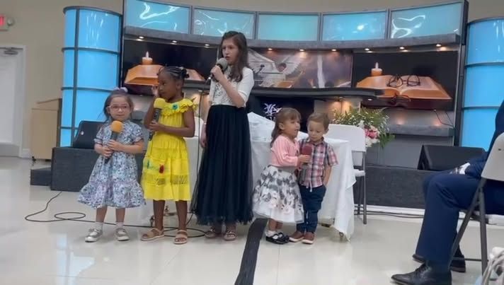 A woman is standing in front of a group of children holding microphones.