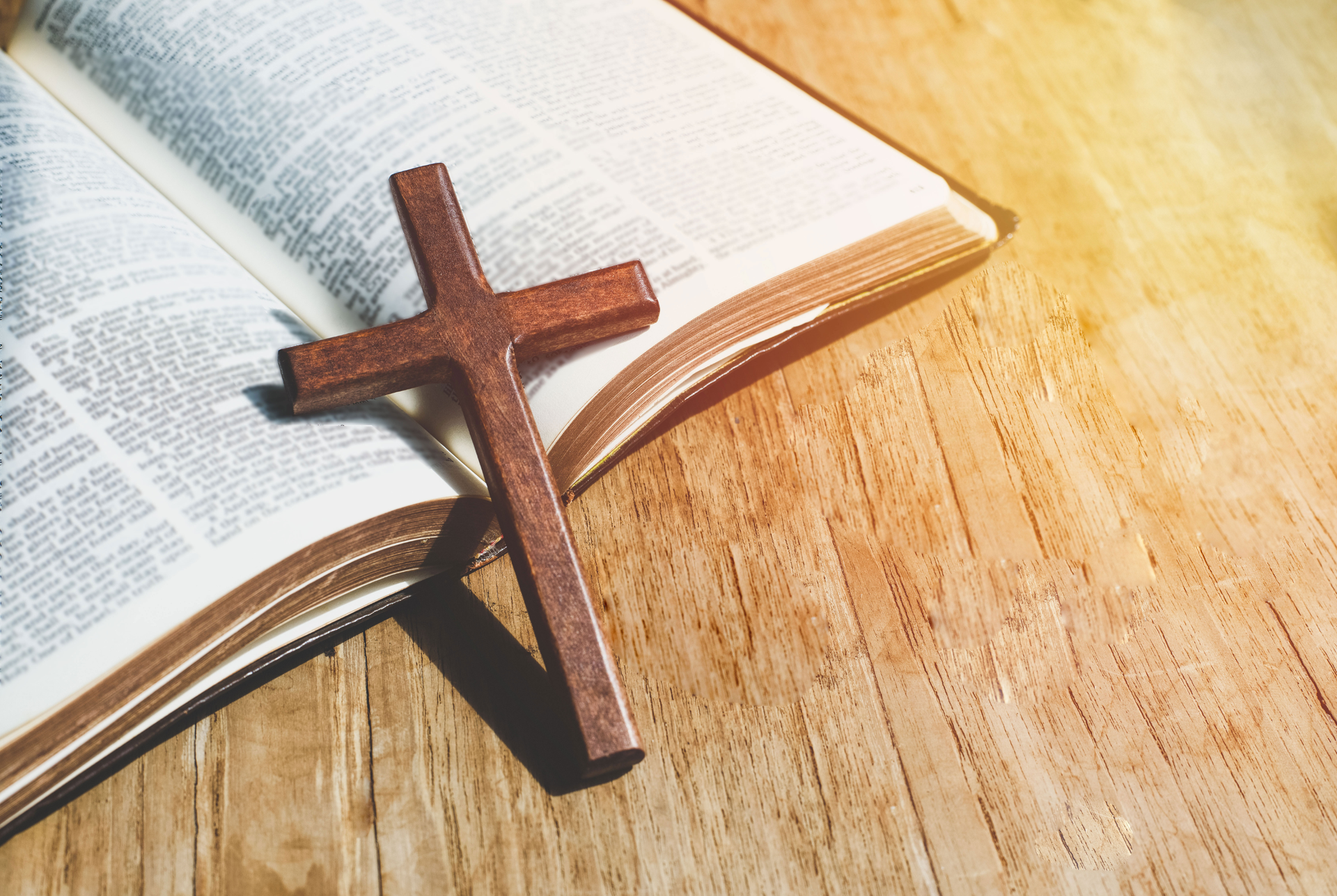 Wooden cross resting on an open Bible on a wooden surface.