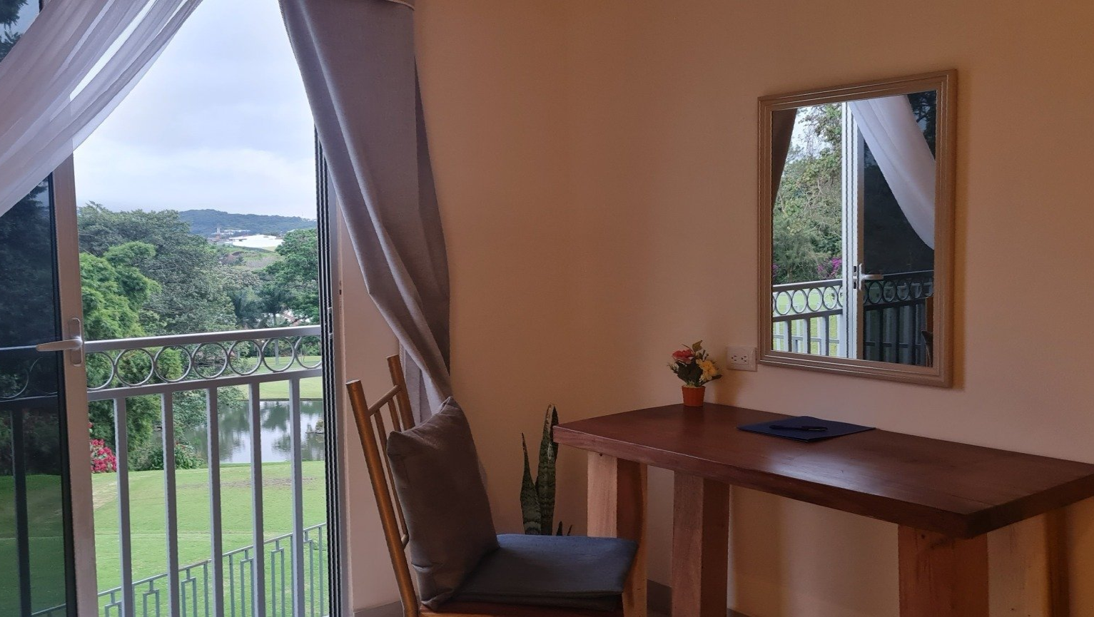 A desk and chair by a window overlooking a green landscape and lake.