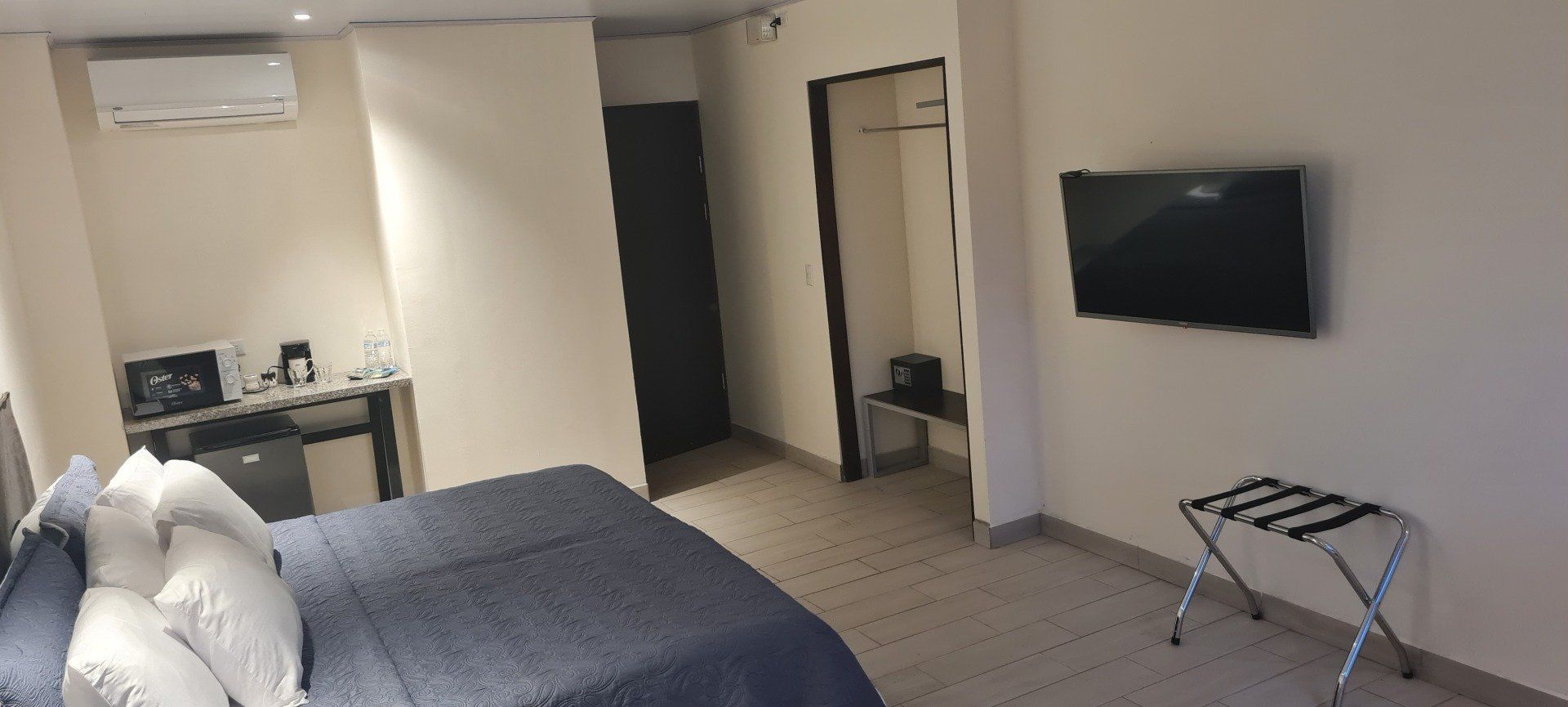 A hotel room with a bed, TV, luggage rack, and kitchenette with coffee maker.