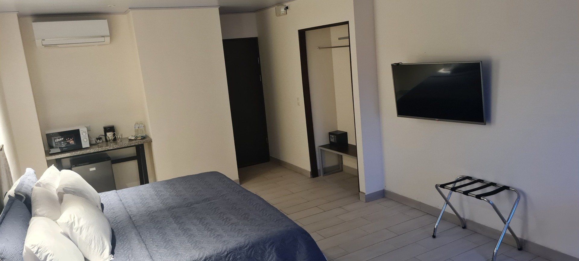 Hotel room with a bed, TV, luggage rack, and mini-fridge.