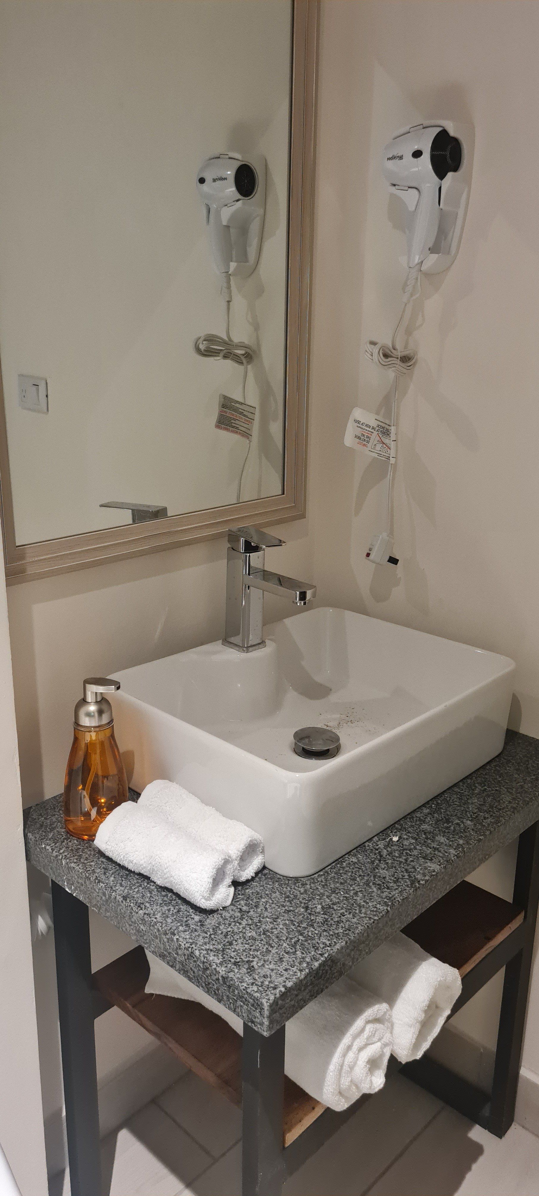 Bathroom with white sink, mirror, and a granite countertop holding towels and soap.