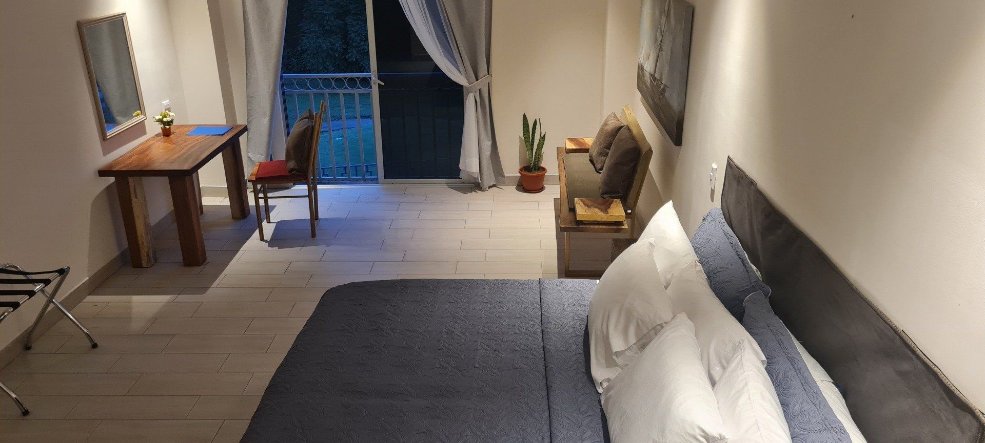 Bedroom with bed, desk, chair, and balcony. White walls, wood floor, and blue and white linens.