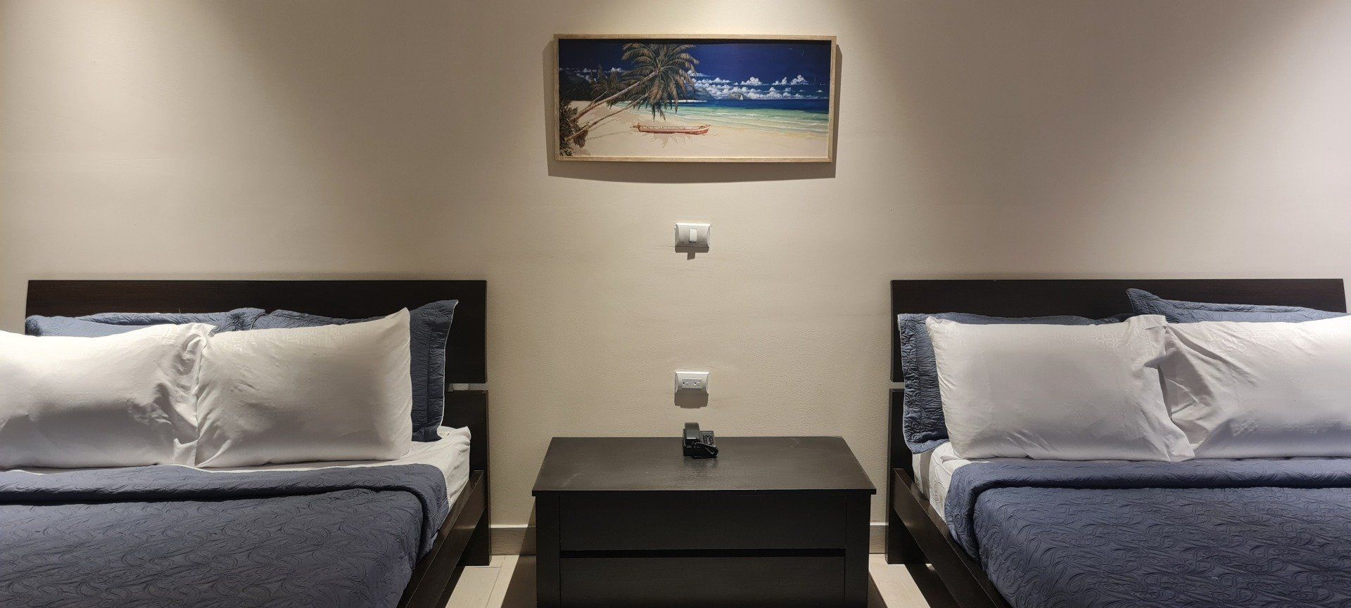 Two beds in a room with a nightstand in between. A painting hangs on the wall above the nightstand.