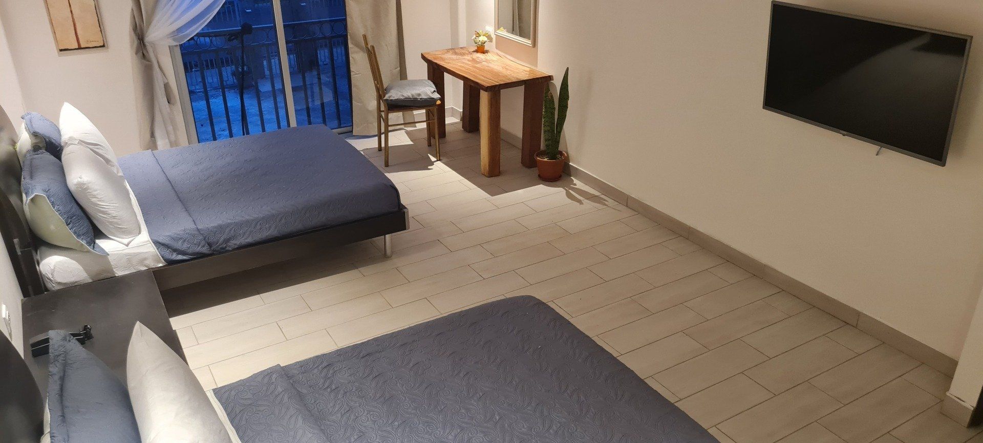 A bedroom with two beds, a table, a chair, and a mounted TV.