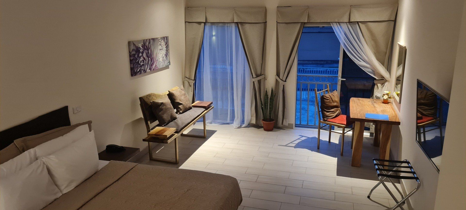 A cozy apartment interior with a bed, bench, table, and balcony entrance.