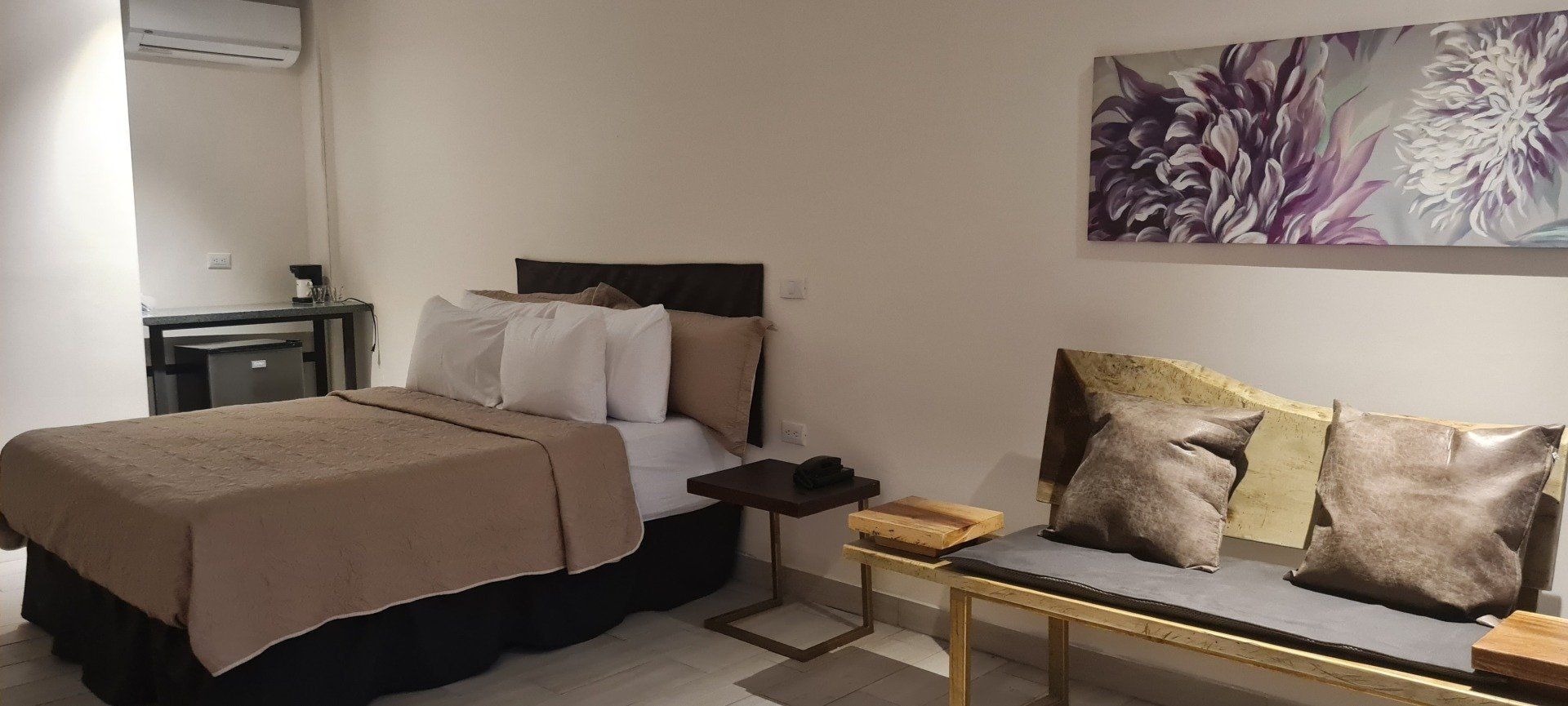 A hotel room with a bed, small sofa, and a wall painting.