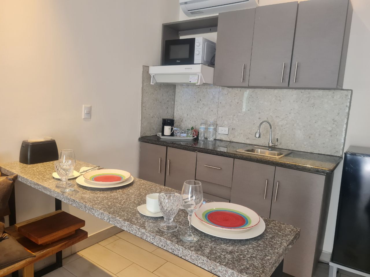 Small kitchen with gray cabinets, microwave, sink, and countertop with place settings.