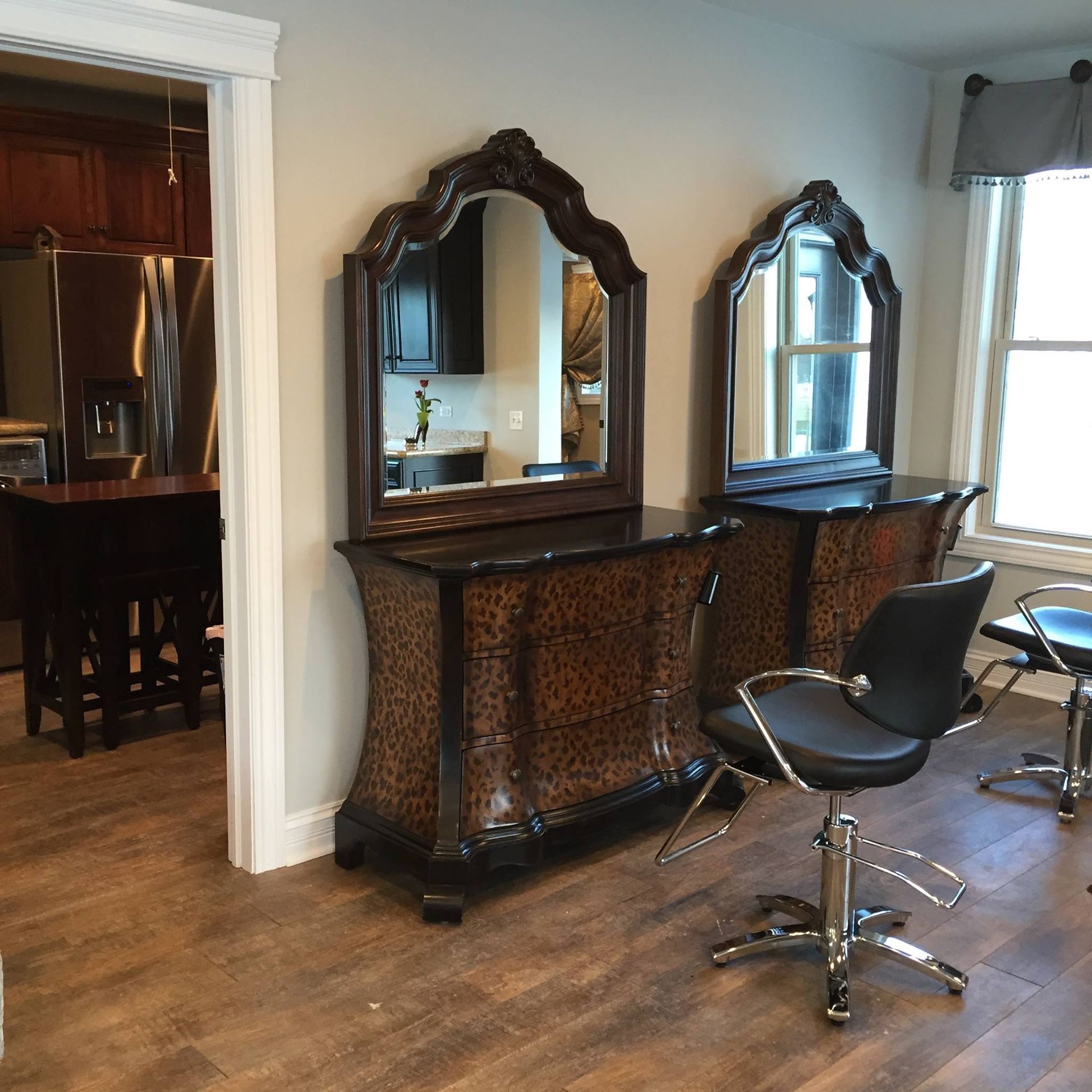 Two leopard-print vanities with large, ornate mirrors and black salon chairs in a wood-floored room.