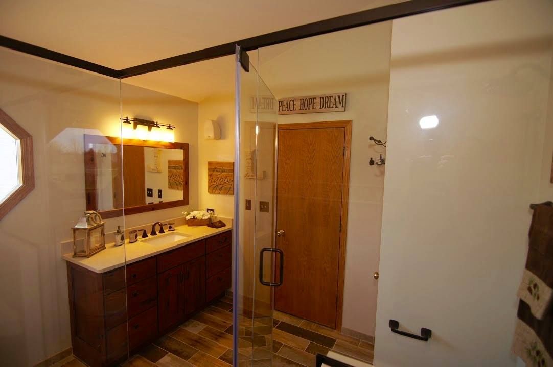 A bright bathroom with a wooden vanity, a large wall mirror, and a glass-enclosed shower with a wooden door.
