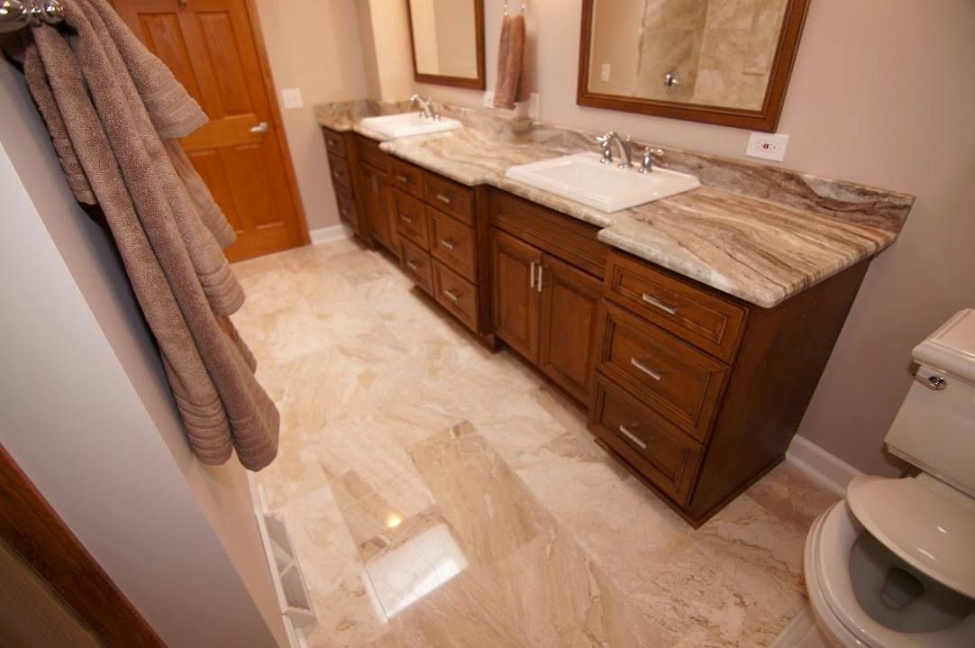 A bathroom with a long wooden double vanity, granite countertops, two sinks, and tiled flooring.