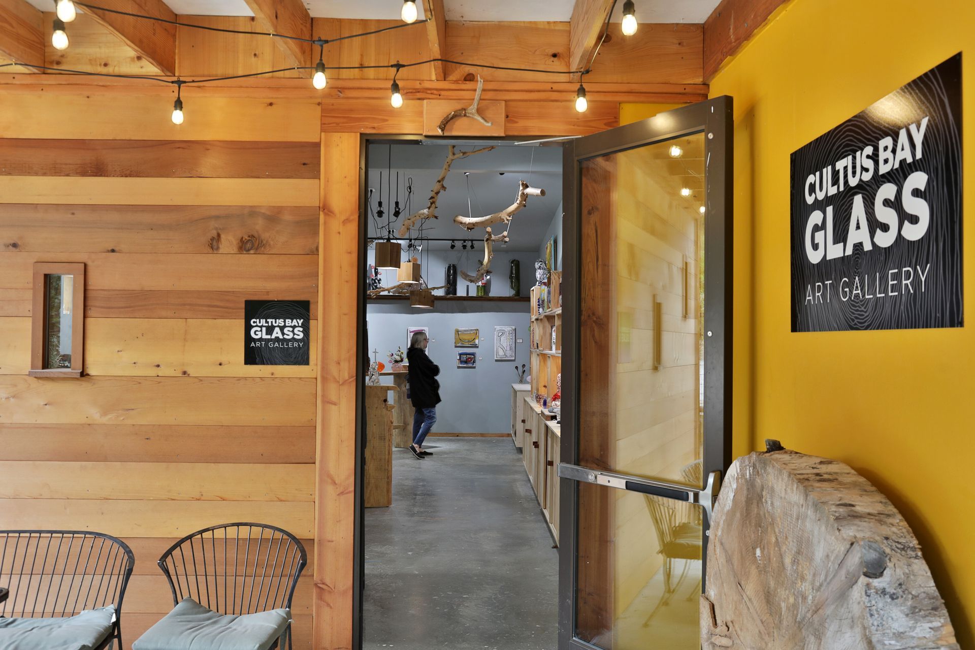 Entrance to Cultus Bay Glass Art Gallery with a person inside, wood paneling, and yellow walls.