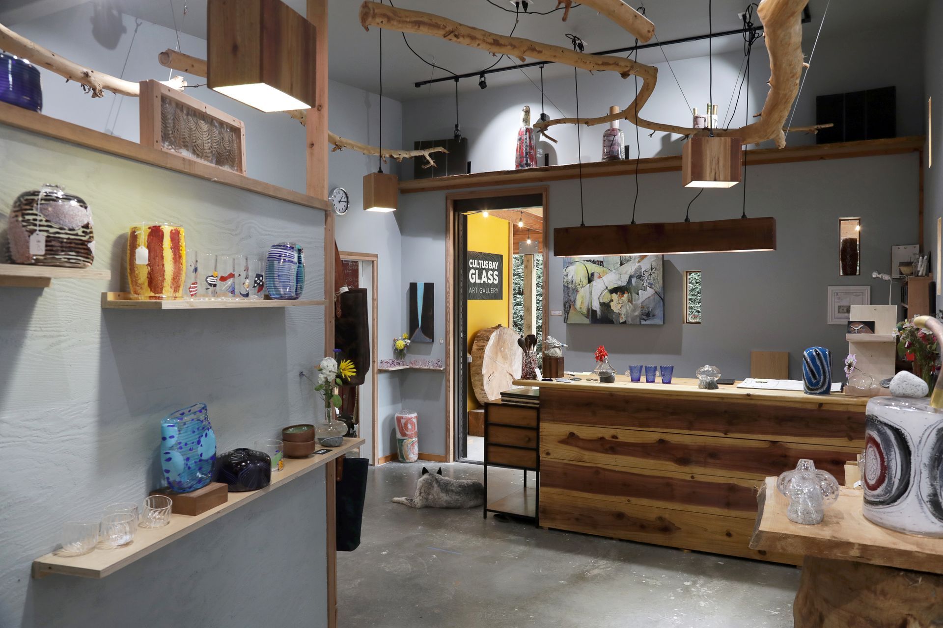 Art gallery interior with glass art on display; a wooden counter and shelves.