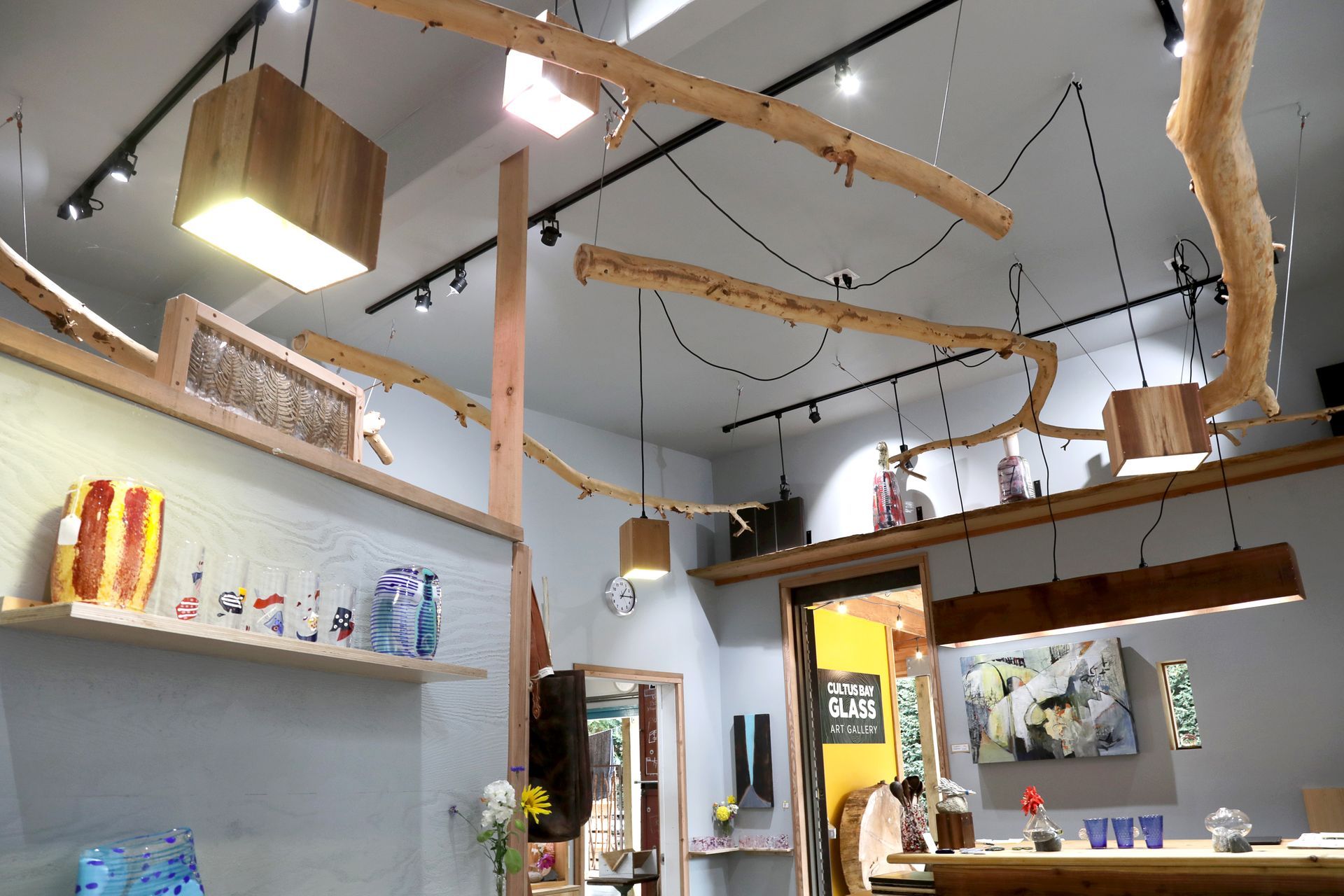 Art gallery interior, featuring wooden light fixtures, artwork displayed on shelves, and an open doorway.