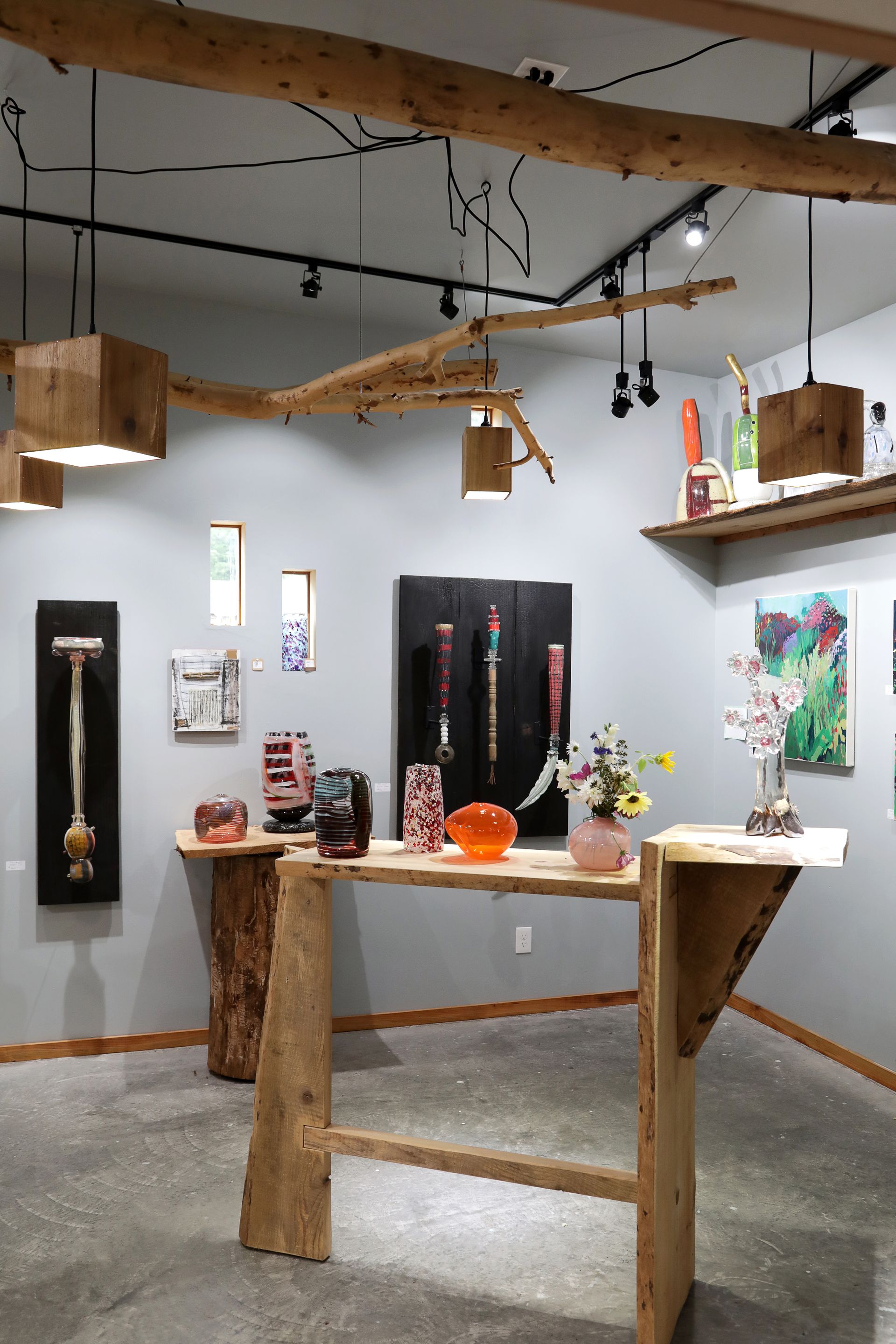 Art gallery interior with wooden sculptures, paintings, and pendant lights.