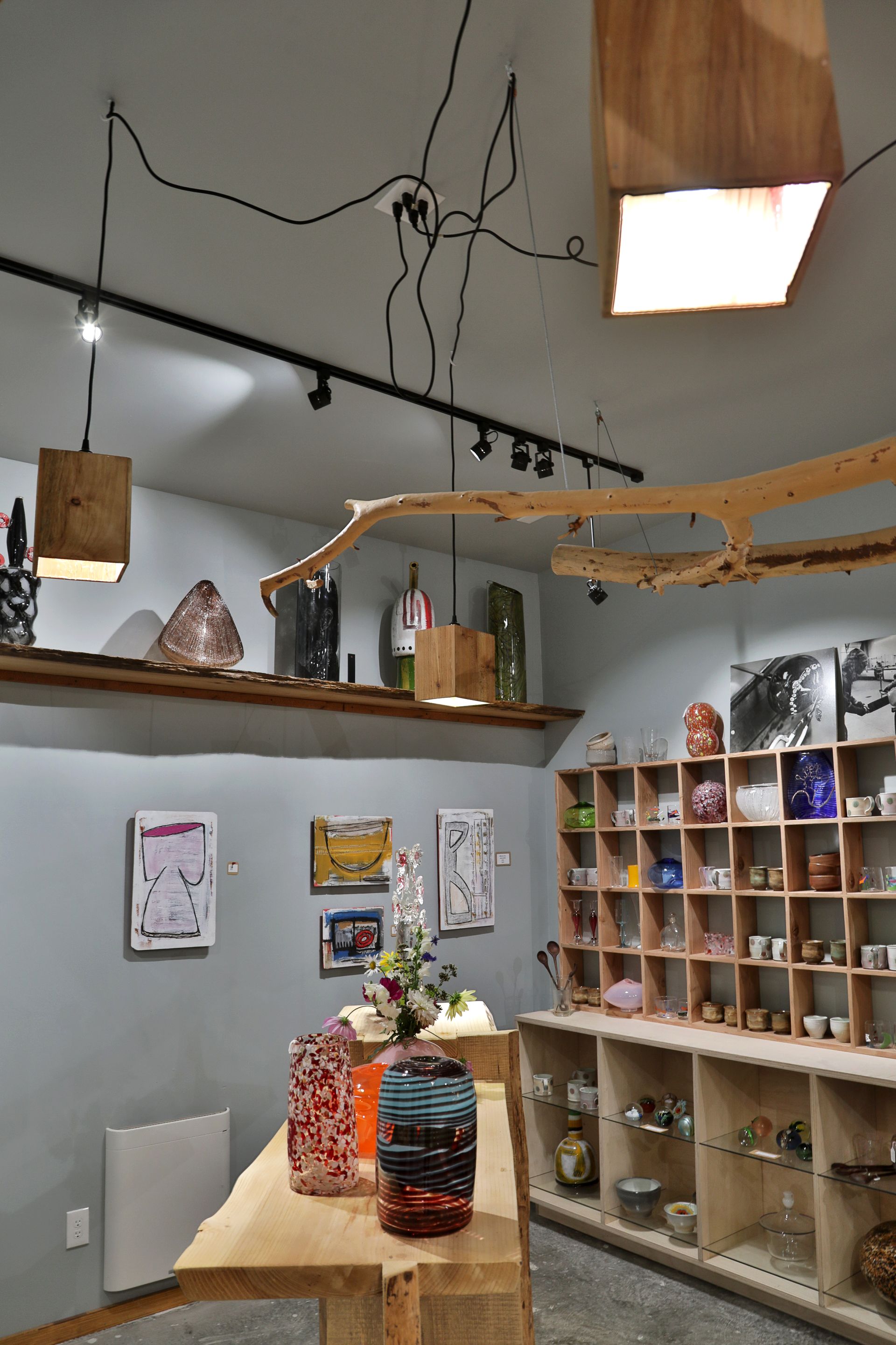 Art gallery interior with wooden shelves, display table, and unique light fixtures.