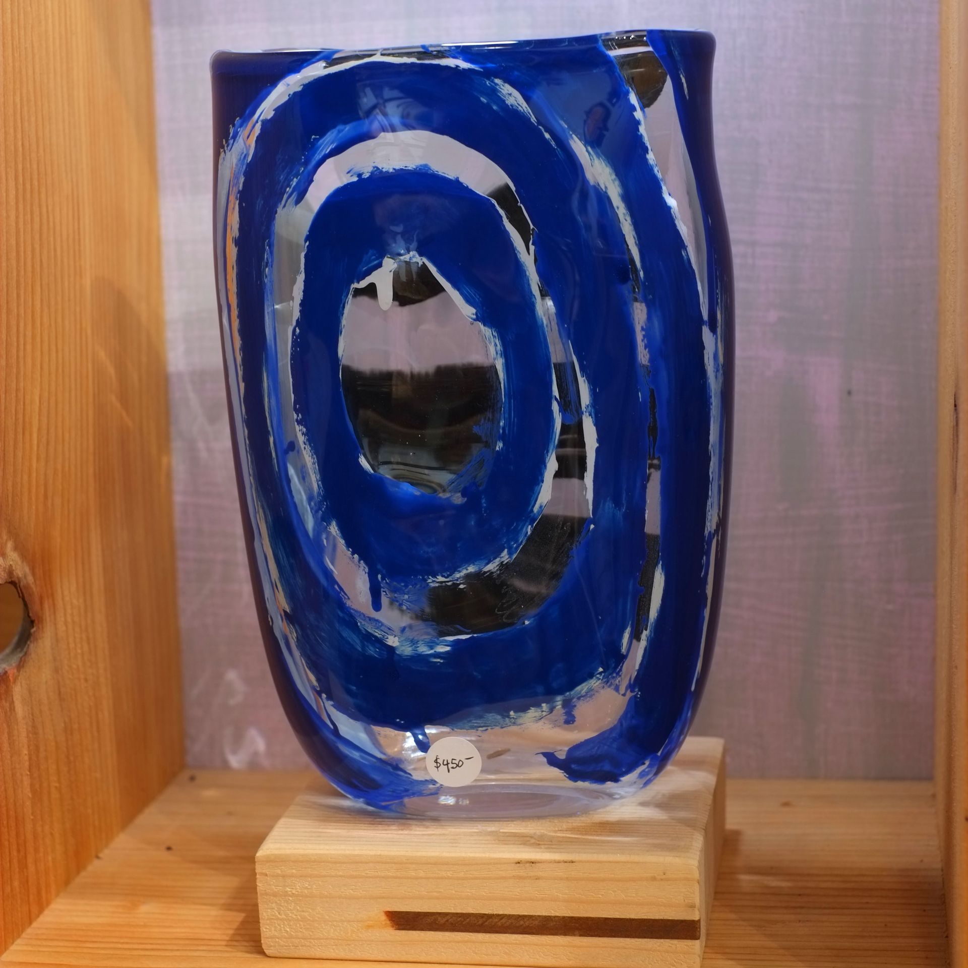 Blue glass vase with a spiral design, resting on a wooden block.