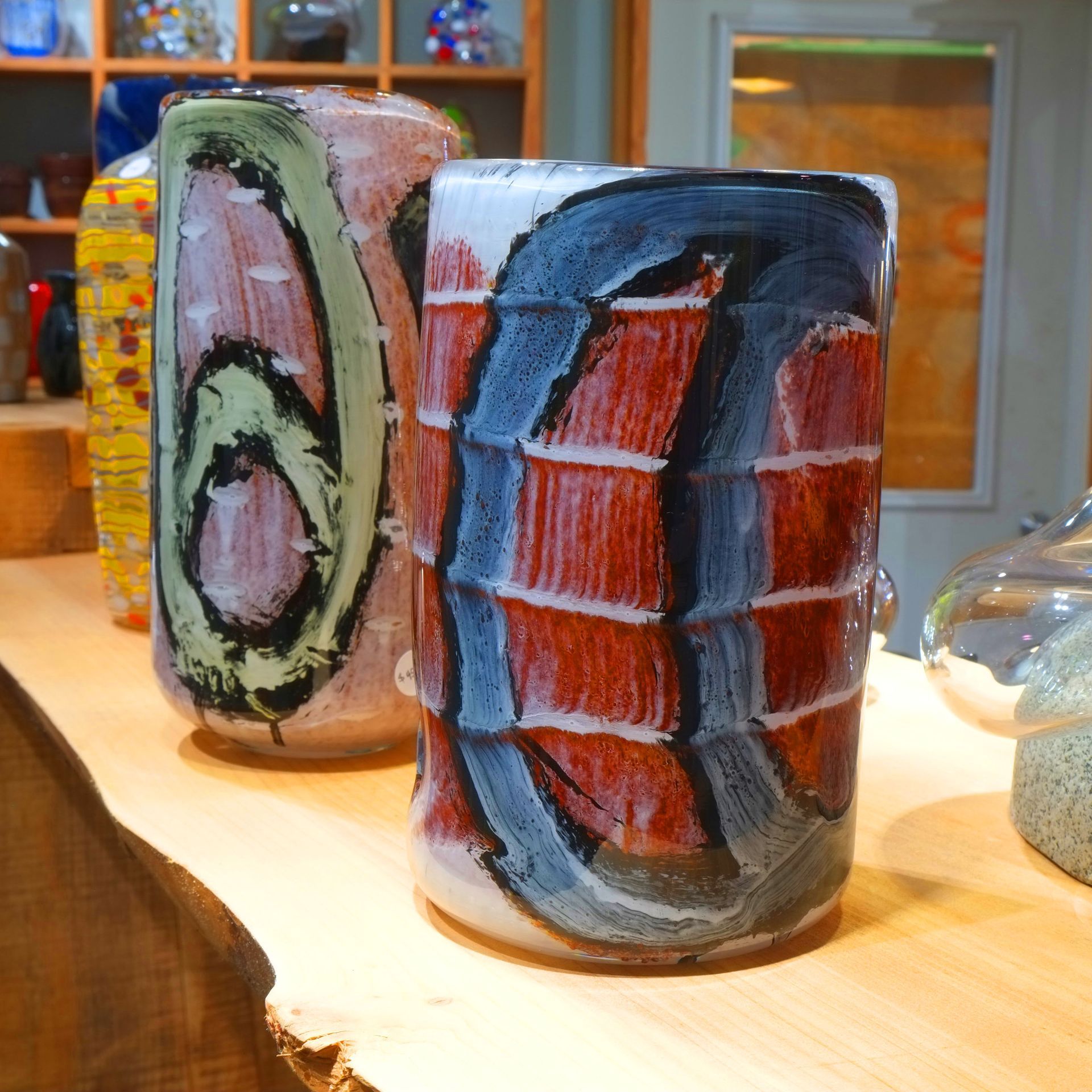 Two colorful glass vases on a wooden surface, with red, blue, and black brushstrokes.