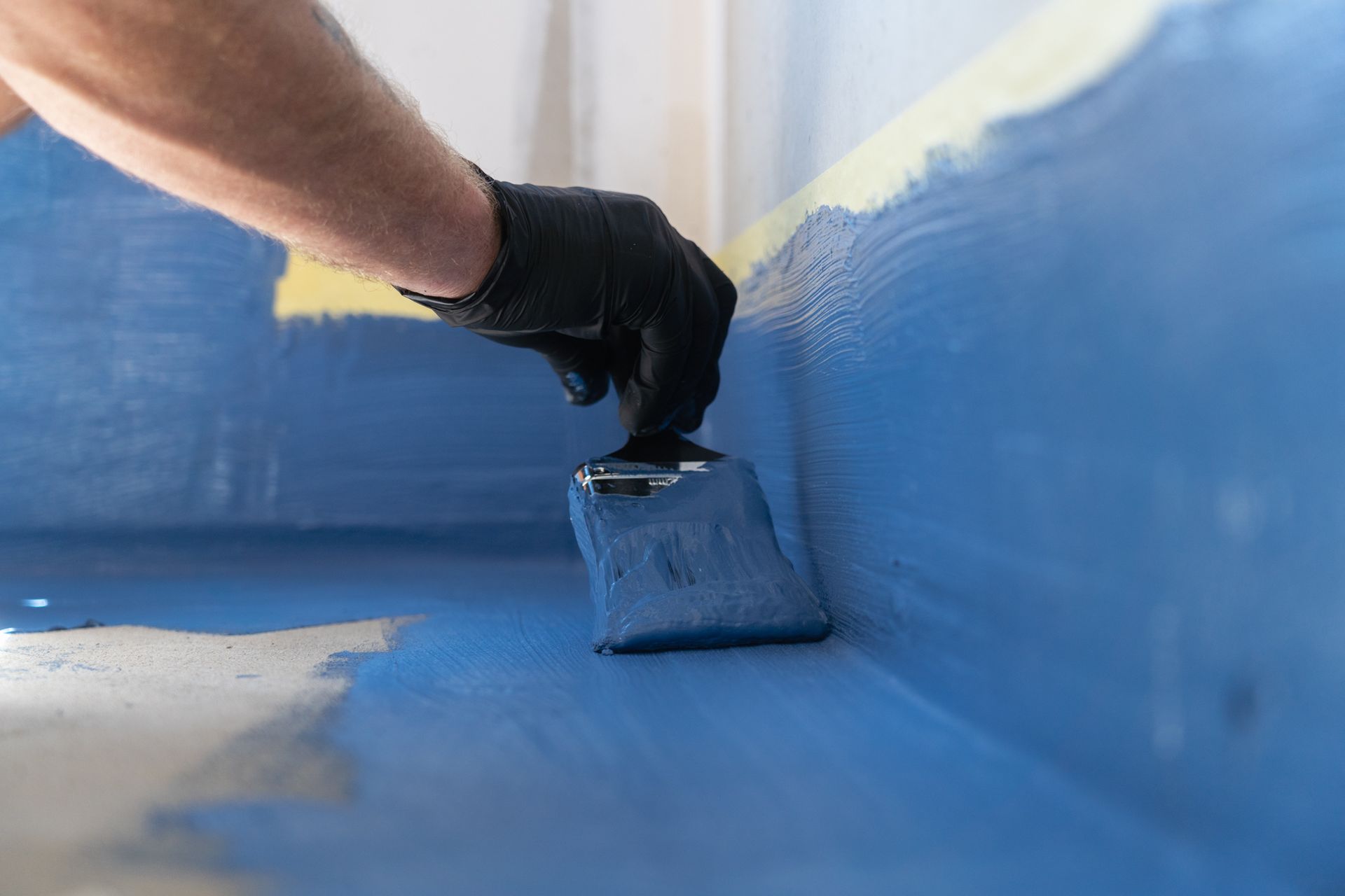 A person is applying blue paint to a wall with a spatula.