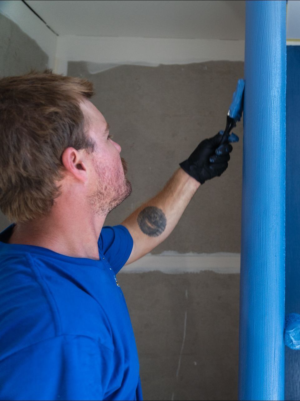 A man in a blue shirt is painting a wall blue