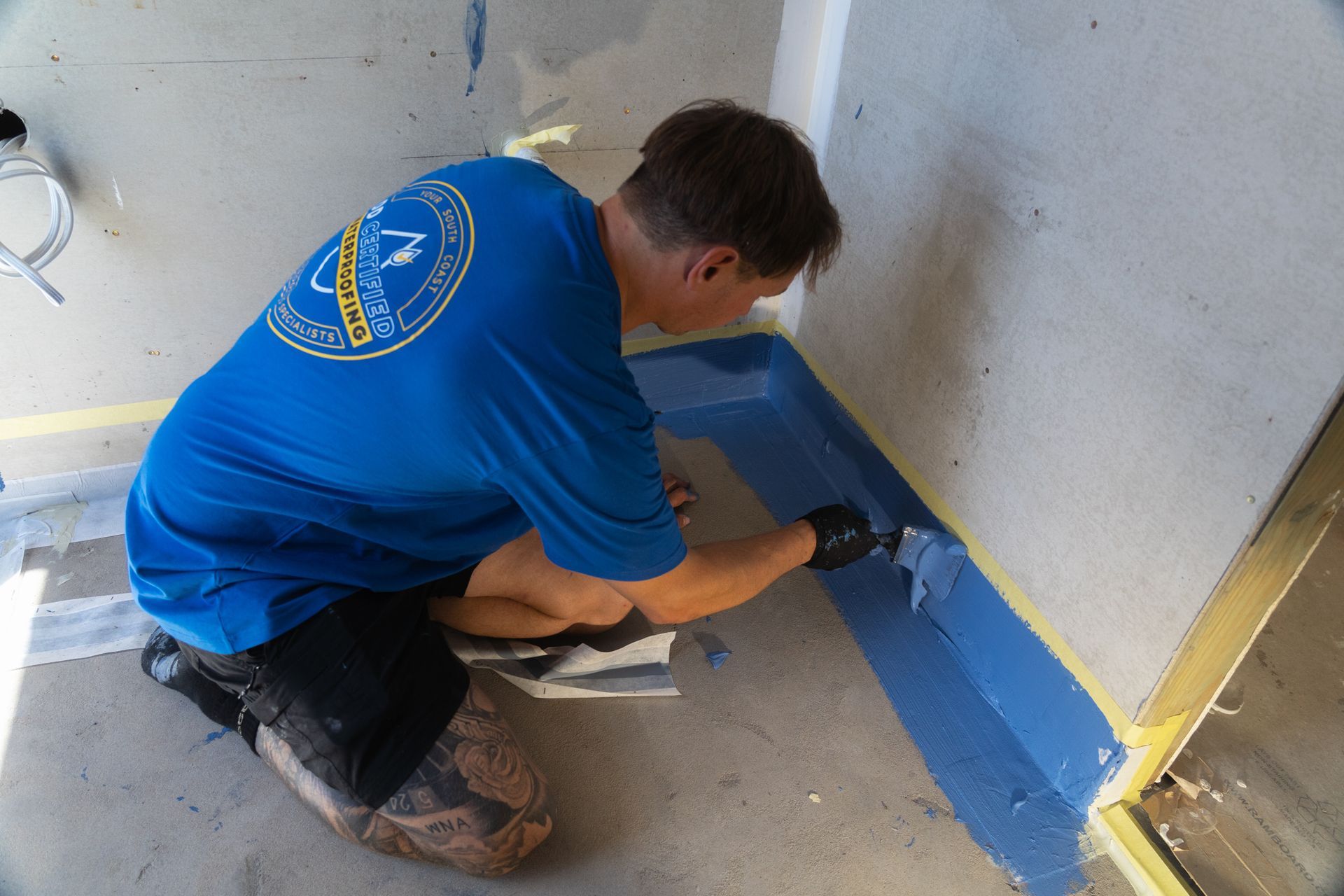 A man in a blue shirt is kneeling down and painting a wall.