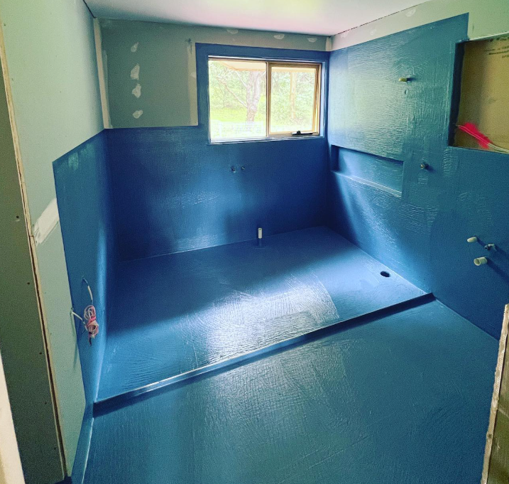 A bathroom under construction with blue walls and a window.