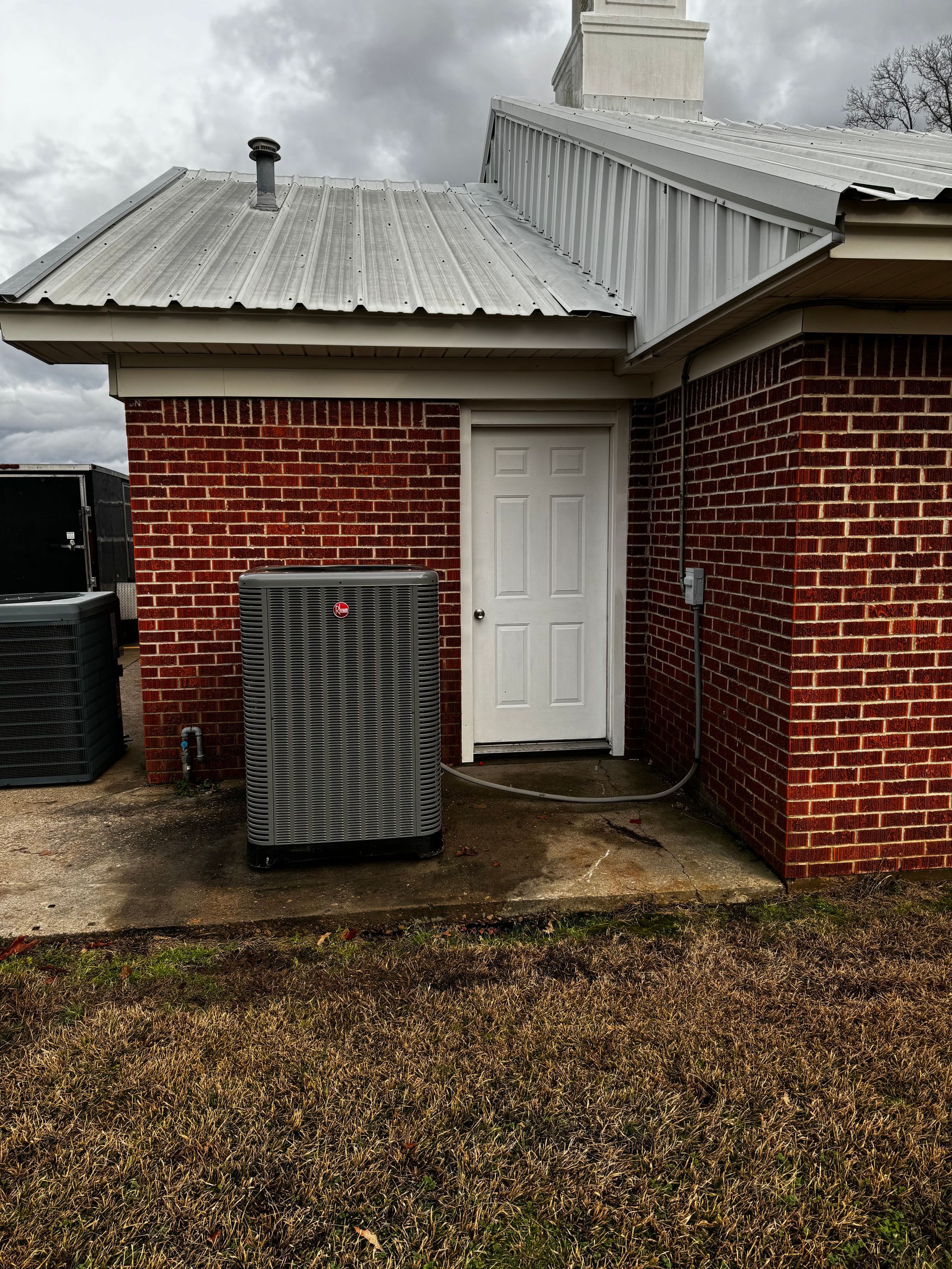 A brick building with a white door and a gray air conditioner.
