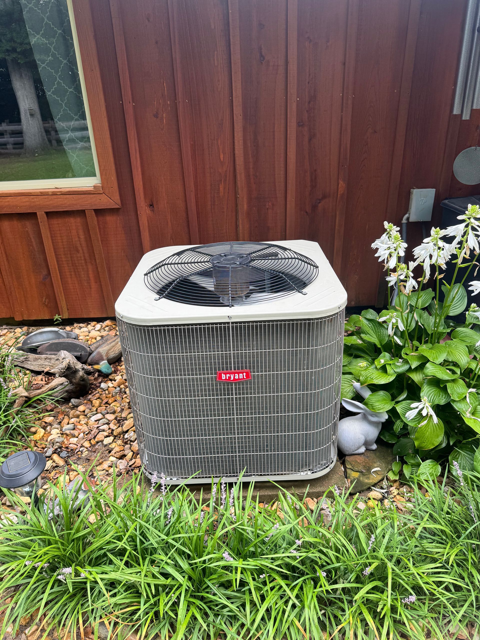 An air conditioner is sitting in the grass in front of a wooden building.