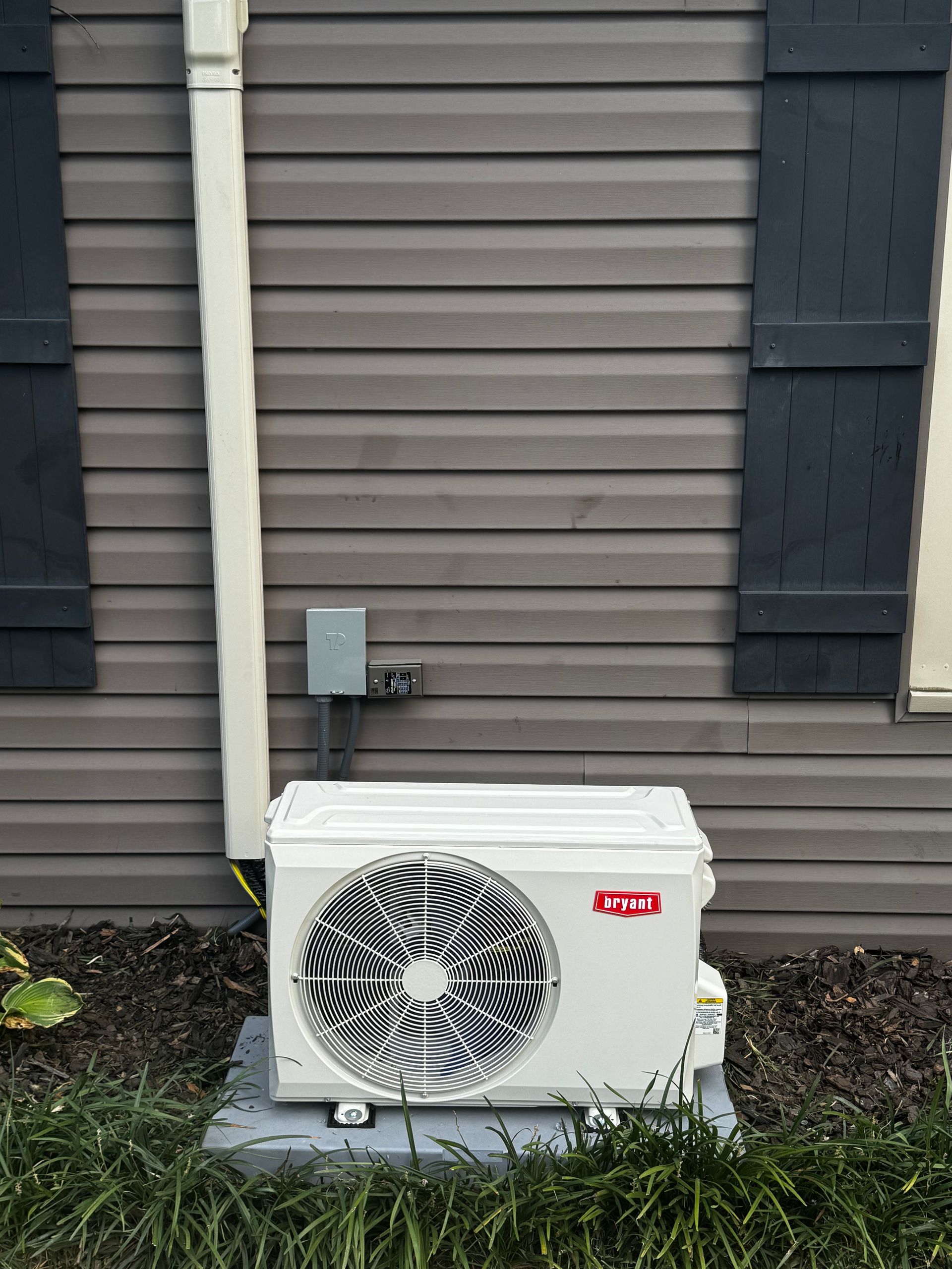 A white air conditioner is sitting outside of a house.