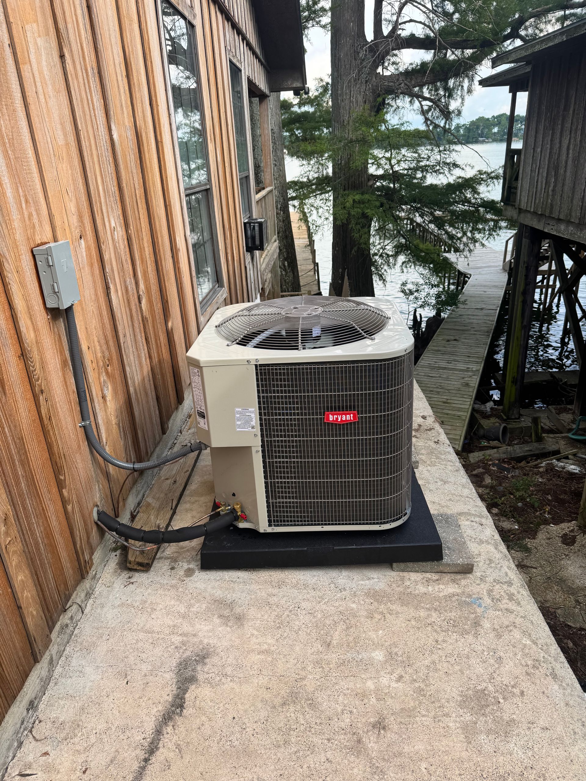 An air conditioner is sitting on top of a concrete ledge next to a wooden building.