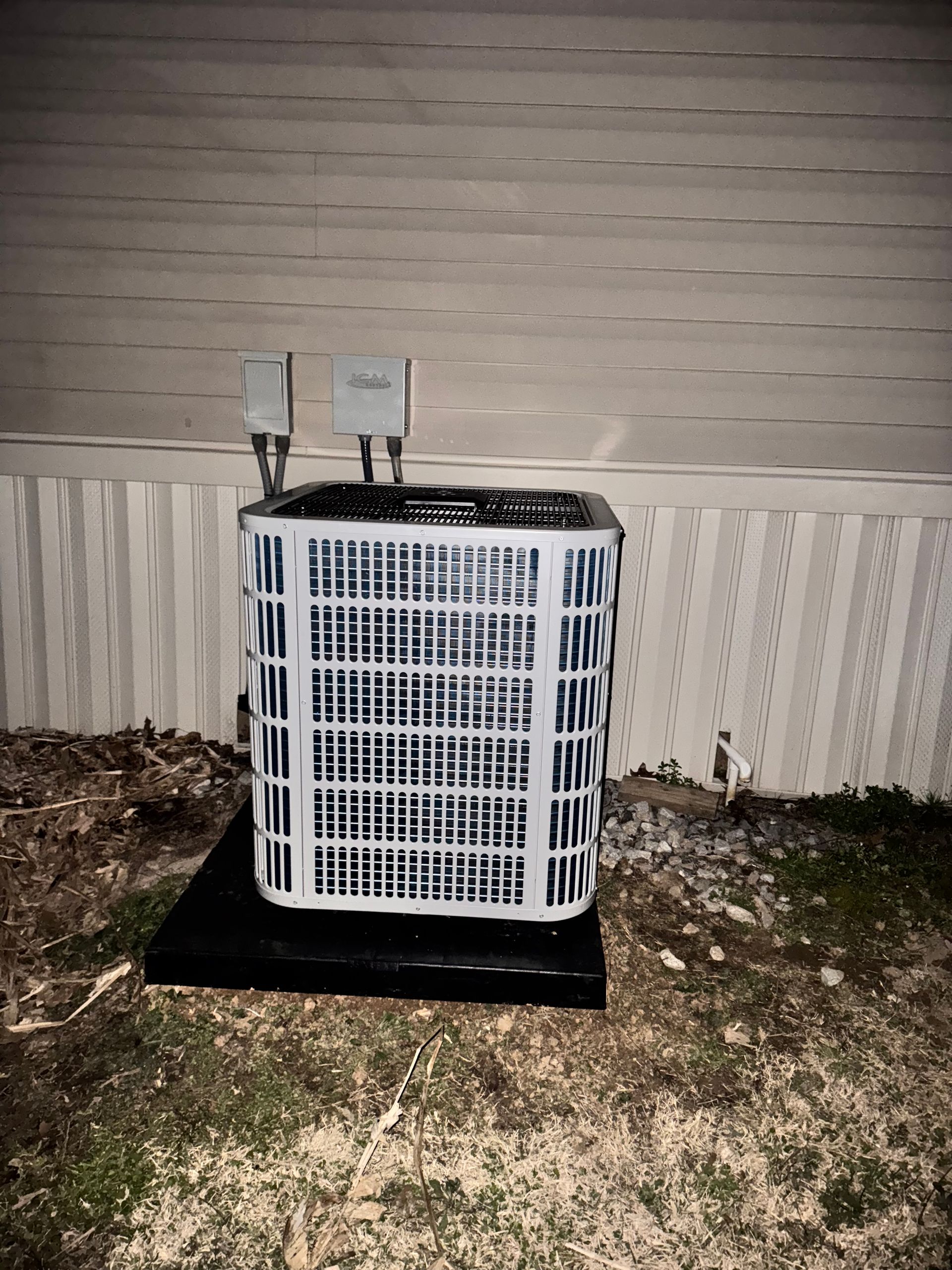 A white air conditioner is sitting on the ground in front of a house.
