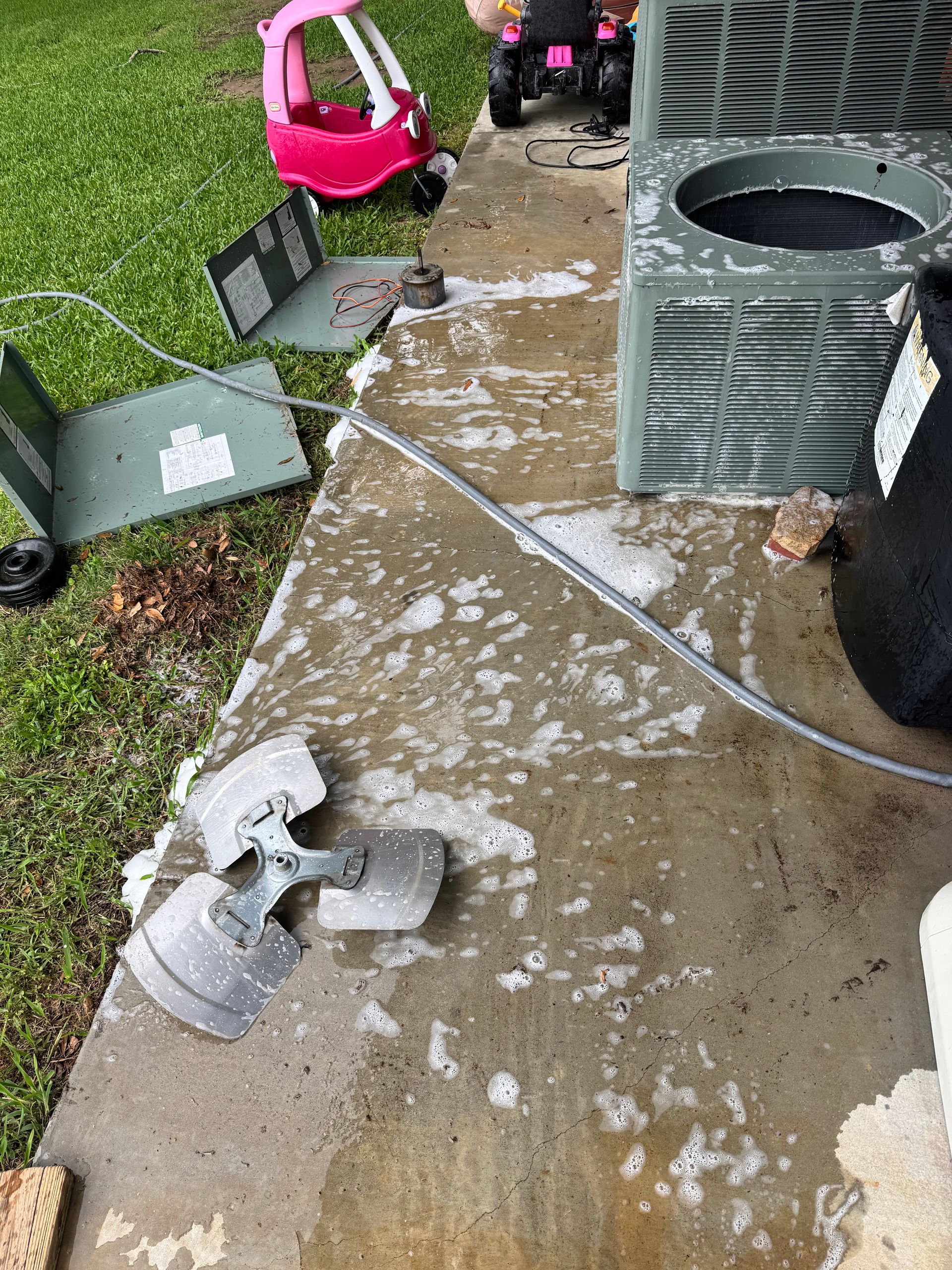 A broken fan is sitting on the ground next to an air conditioner.