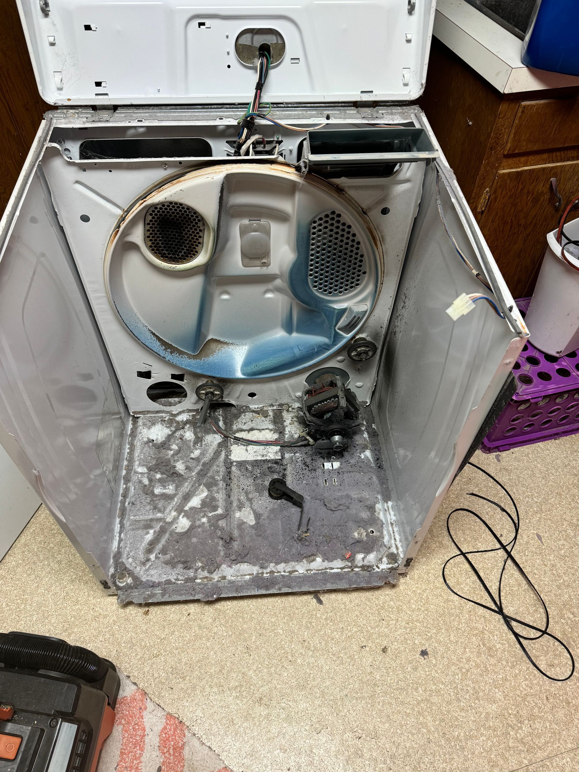 The inside of a broken dryer is sitting on the floor.