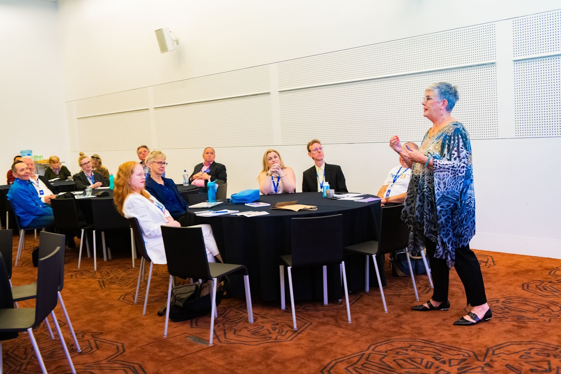 Woman speaking to group seated around a round table in a conference room.