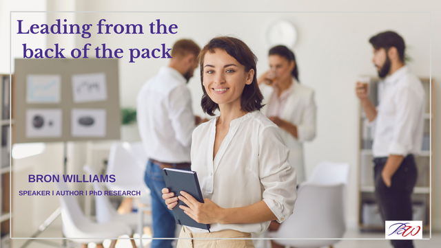 Woman holding a tablet, smiling, in an office setting with colleagues blurred in the background. Text: 