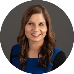 Woman with brown hair smiles, wearing blue and black top, against a gray background.