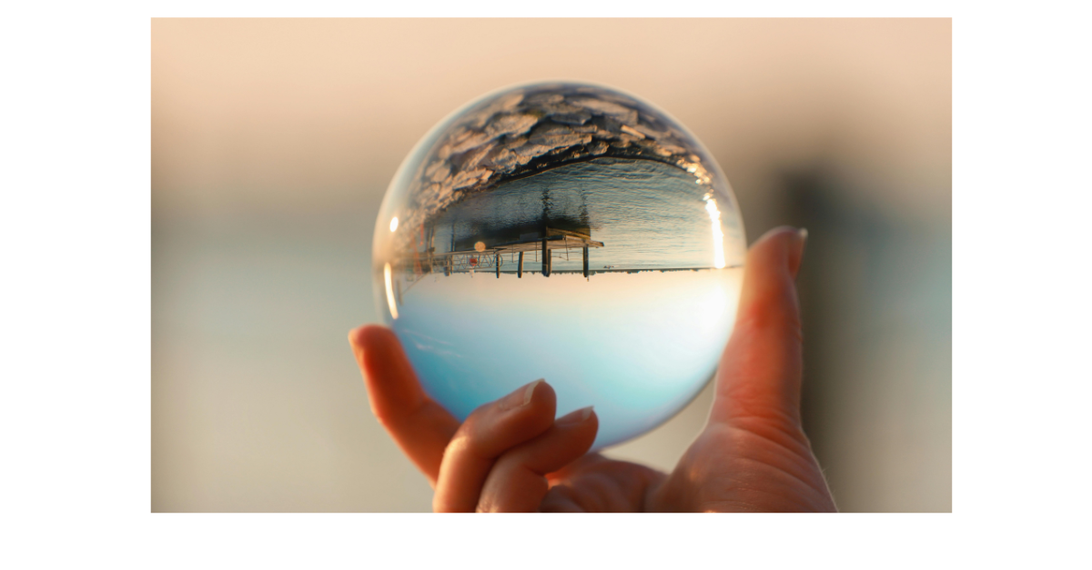 Hand holding a crystal ball, reflecting a cloudy sky and wooden posts over water.