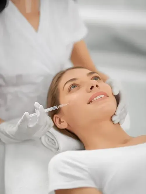 Woman receiving a facial treatment while lying back on a spa bed, with a practitioner applying serum.