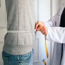 Doctor measuring a person’s waist with a tape measure in a clinic room