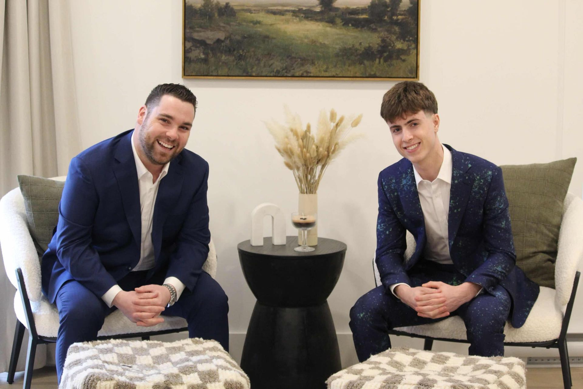 Two men in suits are sitting next to each other in a living room.